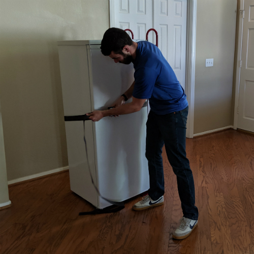 Moving Professional wraps a strap around a freezer to secure it to an appliance dolly