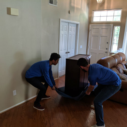 Delivery professionals sliding a cabinet across a wooden floor using a moving blanket