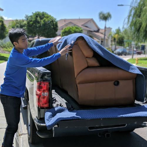 How to Move a Couch - A man in a blue shirt putting a blue moving blanket over the top of a leather couch in a pickup