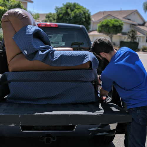 How to Move a Couch - a man in a blue shirt fastening a ratchet strap around a couch in the back of a pickup